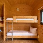 Zimmer mit Doppelstockbett, Holzwand und Fenster.