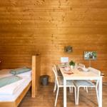 Schlafplatz mit Bett und Esstisch mit Stühlen in Holzhaus.