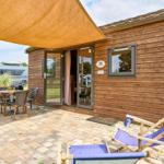 Holzhaus mit Terrasse, Liegestühlen und Grillplatz. Durchgangstür zur Wohnung.