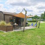 Holzhaus mit Terrasse, Sonnensegel, Grill und Liegestühle im Grün.