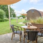 Terrasse mit Tisch und Stühlen unter Markise. Im Hintergrund Grasfläche und Holzhaus.