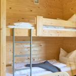 Hochbetten mit Matratzen und Kissen in Holzhaus. Metallleiter und Regal mit Kaffeemaschine.