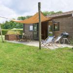 Holzhütte mit Terrasse, Sonnensegel, Liegestühlen und Grill.