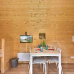 Ein Raum mit Holzwand, Tisch, Stühlen, Bett und Fernseher.