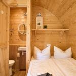 Schlafzimmer mit Holzwand und Bett. Nebenraum mit Toilette und Waschbecken.