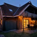 Haus mit Terrasse, Tisch, Stühlen und Lichterkette bei Dämmerung.