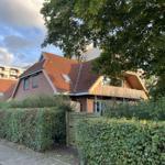 Haus mit rotem Dach und Holzveranda hinter grüner Hecke