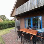 Terrasse mit Tisch, Stühlen und Hochstuhl vor rotem Backsteinhaus mit blauen Fenstern.