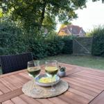 Holztisch mit zwei Weingläsern, Schale und Pflanze im Garten.