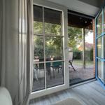 Durch die Glastüren ist der Garten mit Tisch und Stühlen zu sehen.