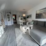 Wohnzimmer mit Sofa, Couchtisch und Fernseher. Im Hintergrund Essbereich und Schlafzimmer.