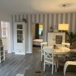 Essbereich mit runden Tisch und weißen Stühlen. Hintergrund mit Streifenwand und Blick in Schlafzimmer.