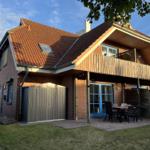 Haus mit Terrasse, Garten und Holzveranda. Blaue Fenster und rote Dachziegel.