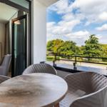 Terrasse mit Tisch und Stühlen. Blick auf grüne Bäume und einen See.