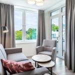 Wohnzimmer mit Sofa, Sessel und Tisch. Fenster und Balkontür bieten Blick auf Grün.