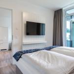 Schlafzimmer mit Bett, TV und Blick auf Balkon. Küche im Hintergrund.