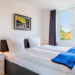 Schlafzimmer mit Bett, Nachttisch und Fensterblick auf Wald.