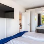 Schlafzimmer mit Bett, TV und Spiegelschrank. Durchgang zu Arbeitsbereich.