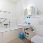 Badezimmer mit Badewanne, Waschbecken und Toilette. Blaue Accessoires und Handlauf.