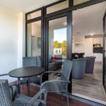 Terrasse mit Tisch und Stühlen. Durch Glastüren ist Wohn- und Küchenbereich sichtbar.