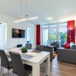 Wohn- und Essbereich mit TV, Esstisch und Balkonansicht.