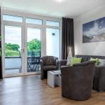 Wohnzimmer mit Sofa, Sessel und Balkonansicht.