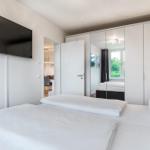 Schlafzimmer mit Bett, Spiegelschrank und Wandfernseher. Blick in die Küche.