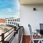 Terrasse mit Tisch und Stühlen. Blick auf moderne Gebäude und Park.