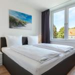 Schlafzimmer mit Doppelbett, Nachttisch und Fensterblick auf Dach und Bäume.