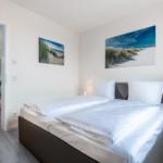 Schlafzimmer mit Doppelbett, Wandbildern und Sicht in die Küche.