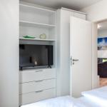 Schlafzimmer mit weißem Schrank, Fernseher und Blick in Wohnzimmer.