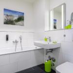 Badezimmer mit Badewanne, Waschbecken und Toilette. Grüne Accessoires und Spiegel.