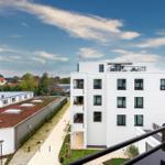 Moderne weiße Wohnanlage mit Balkonen und grünen Flächen unter blauem Himmel.