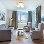 Wohnzimmer mit Sofa, zwei Sesseln, TV und Fenster mit Blick.