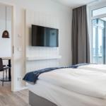 Schlafzimmer mit Doppelbett, TV und Blick auf Balkon. Nebenraum mit Tisch und Stühlen.