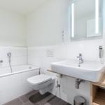 Badezimmer mit Badewanne, Toilette und Waschbecken mit beleuchtetem Spiegel.