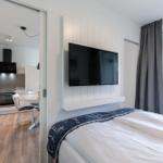 Schlafzimmer mit TV und Blick auf Balkon. Küche im Hintergrund sichtbar.