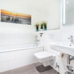 Badezimmer mit Badewanne, Waschbecken und Toilette. Wandbild und Pflanzen sichtbar.