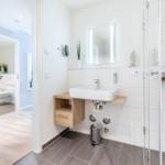 Badezimmer mit Dusche, Waschbecken und Spiegel. Tür führt in Toilettenraum.