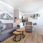 Wohnzimmer mit Sofa, Sessel und Küchenbereich. Holzboden und Wandbild.