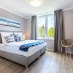 Schlafzimmer mit Bett, Fenster und TV. Holzboden und graue Wände.