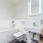 Badezimmer mit Badewanne, Toilette und Waschbecken mit beleuchtetem Spiegel.