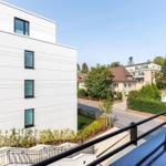 Blick von Balkon auf moderne Wohnanlage und grüne Umgebung mit Straßen und Häusern.