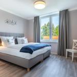 Schlafzimmer mit Doppelbett, Fenster, TV und Stuhl.