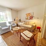 Wohnzimmer mit Sofa, Sesseln und Teppich. Wandbild und Fenster mit Blick nach draußen.