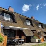 Dorfhaus mit Strohdach, Terrasse und Gartenmöbel unter blauem Himmel.