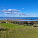 Panorama über Felder, Häuser und Meer unter blauem Himmel mit weißen Wolken.