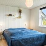 Schlafzimmer mit blauer Bettdecke, Holzboden und Fenster mit Blick auf Grün.