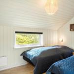 Zwei Betten mit blauen Decken, Fenster mit Blick auf Grün, weiße Wände und Holzboden.