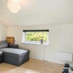 Ein Wohnzimmer mit grasem Sofa, Fenster und Fernseher an der Wand.